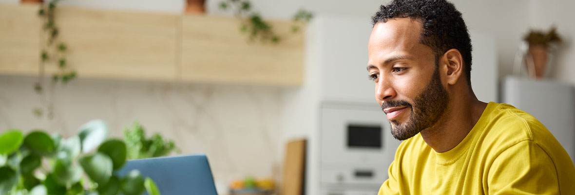 1. A man wearing a yellow shirt is focused on his laptop screen, engaged in work or research.