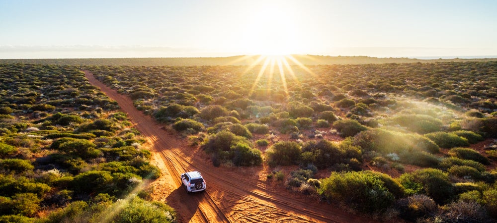 An image of a car driving down a road in a remote part of the Northern Territory.