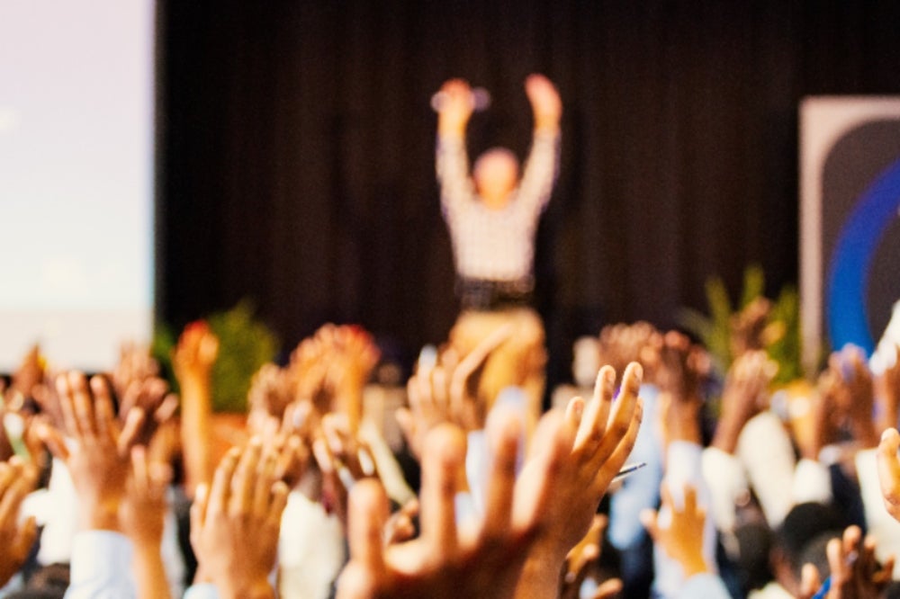 Blurred image of people raising their hands in an auditorium.