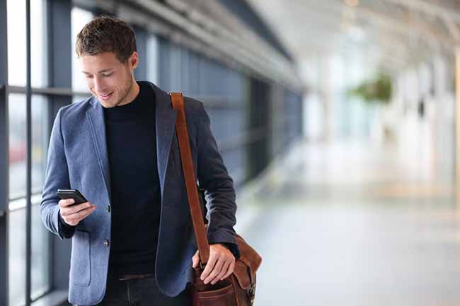 A man in a business suit walking through a hallway while using his phone.