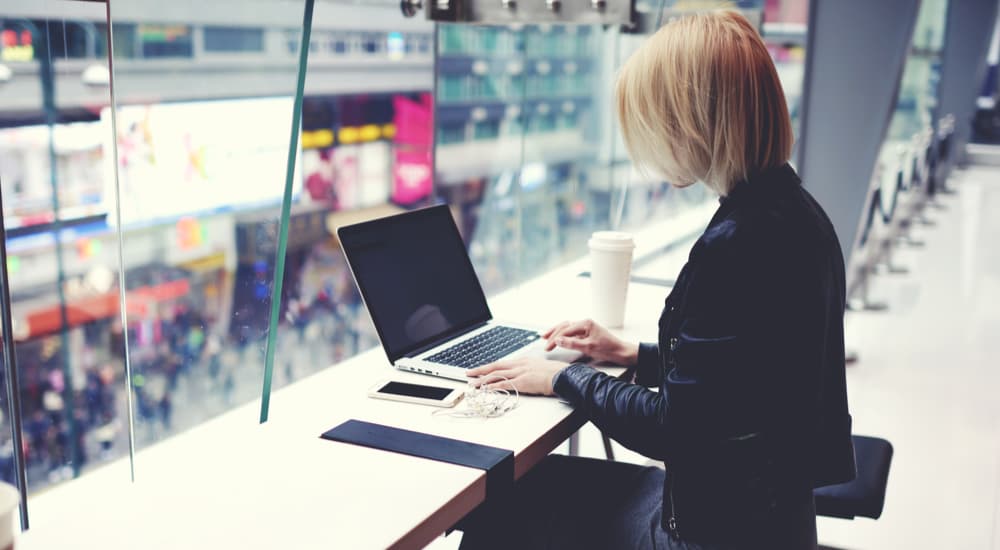 Online MBA student catching up with some reading on her laptop in an airport departures lounge. 