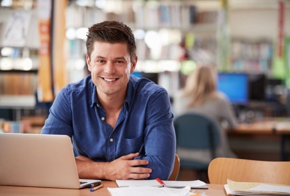 A VU Online Master of Financial Planning student sits smiling at a table with a laptop and documents.