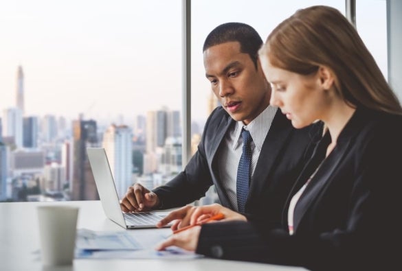 Two financial planners sit at a desk and discuss their work.
