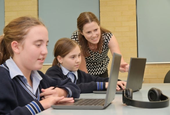 A primary school teacher with a student, pointing at something on their laptop.