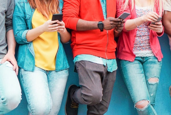 A group of teenagers scrolling on their phone while leaning against a wall.