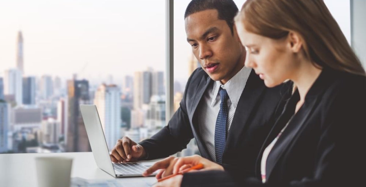 Two financial planners sit at a desk and discuss their work.