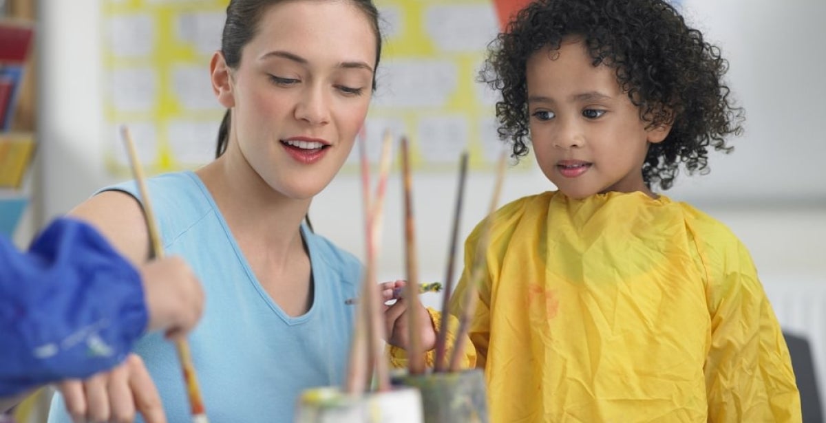 A primary school teacher teaching a student to paint.