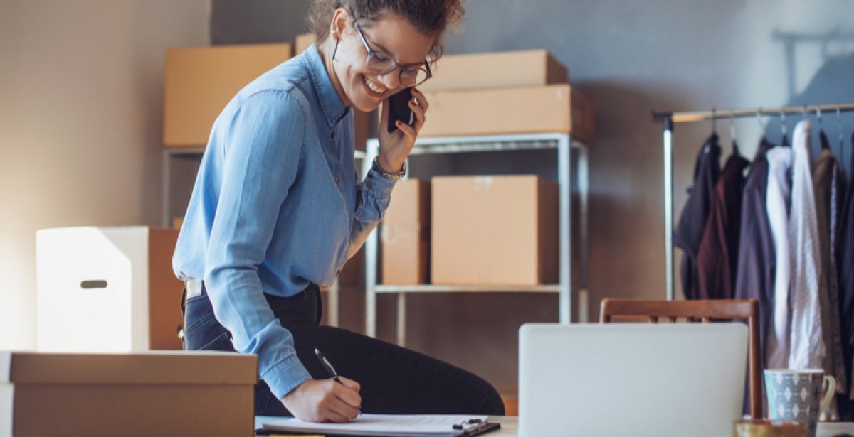 A VU Online MBA student smiles and talks on the phone at their desk.