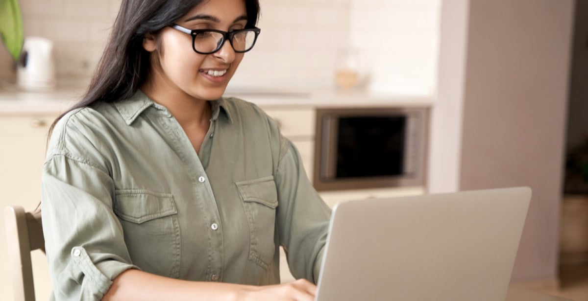 A VU Online Master of Public Health student is sitting at a table, working on her laptop and smiling.