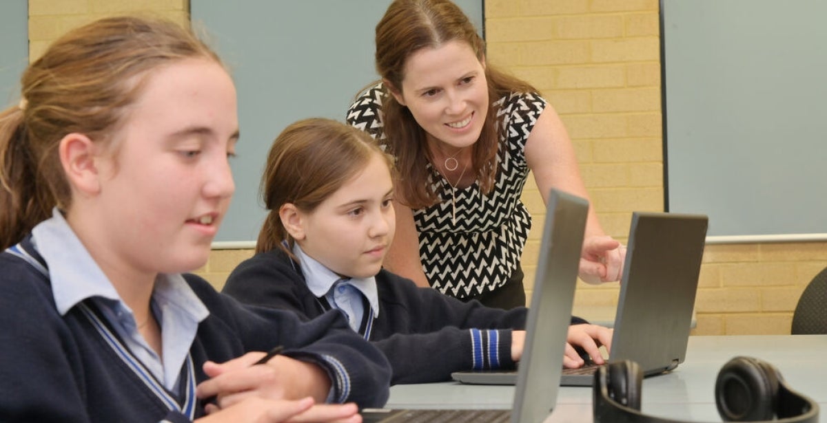 A primary school teacher with a student, pointing at something on their laptop.