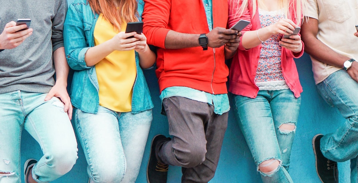 A group of teenagers scrolling on their phone while leaning against a wall.