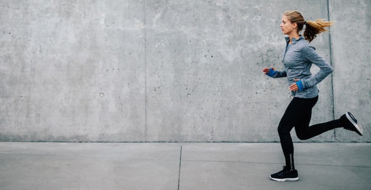 A woman training for a marathon - she is running past a concrete block. 