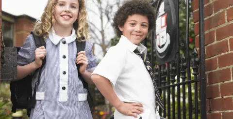 Two students wearing school uniforms smiling outdoors.