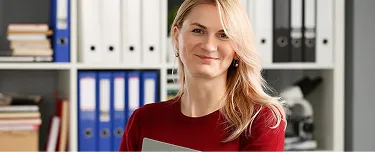 1. A woman wearing a red sweater is holding a laptop, looking engaged and focused on the screen.