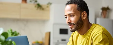 1. A man wearing a yellow shirt is focused on his laptop screen, engaged in work or research.