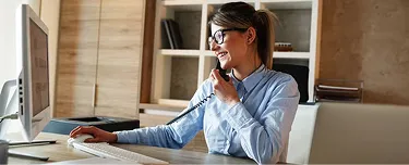 1. A woman in a blue shirt sits at a desk, focused on her computer screen.