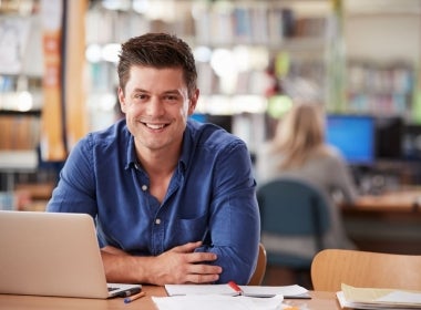 A VU Online Master of Financial Planning student sits smiling at a table with a laptop and documents.