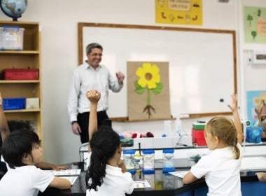 A primary school teacher stands at the front of the classroom.