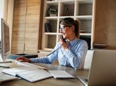 An investment banker busy working on their desk and talking on the phone.