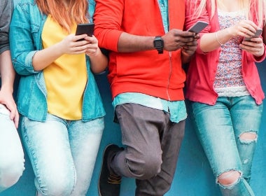 A group of teenagers scrolling on their phone while leaning against a wall.